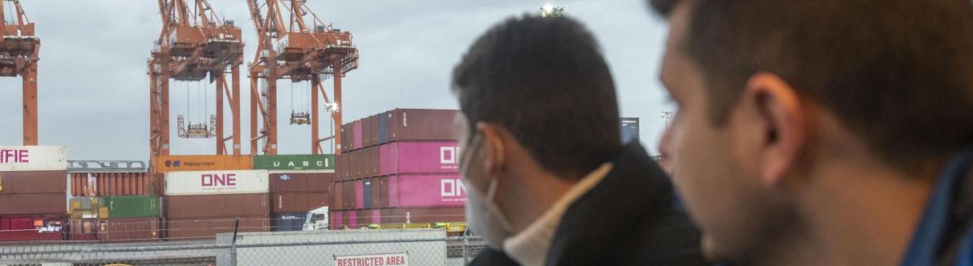 Two men looking out a bus window at some cranes. 