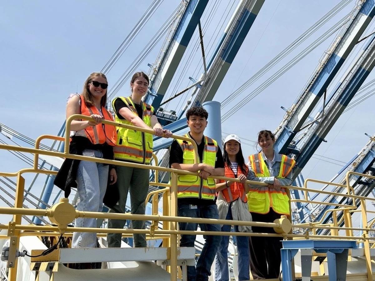 Five young people in safety vests stand on a crane.