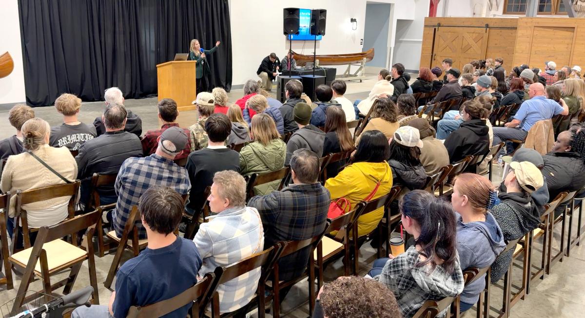 A group of people listen to a speaker talk at an event.