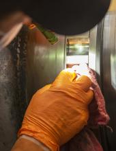 A maintenance worker wearing orange gloves uses a cloth to clean a piece of a equipment.