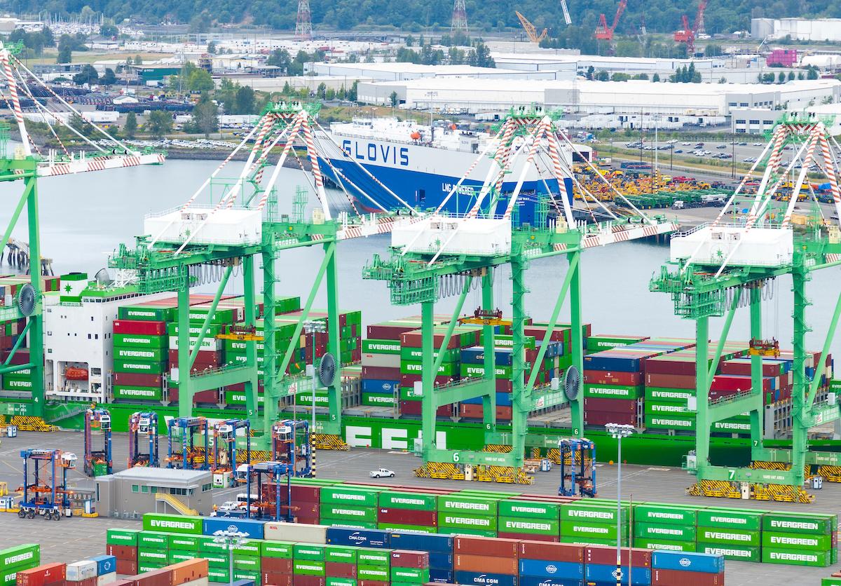 Drone shot of cargo operations and container ships at a Port with a ship in the background. 