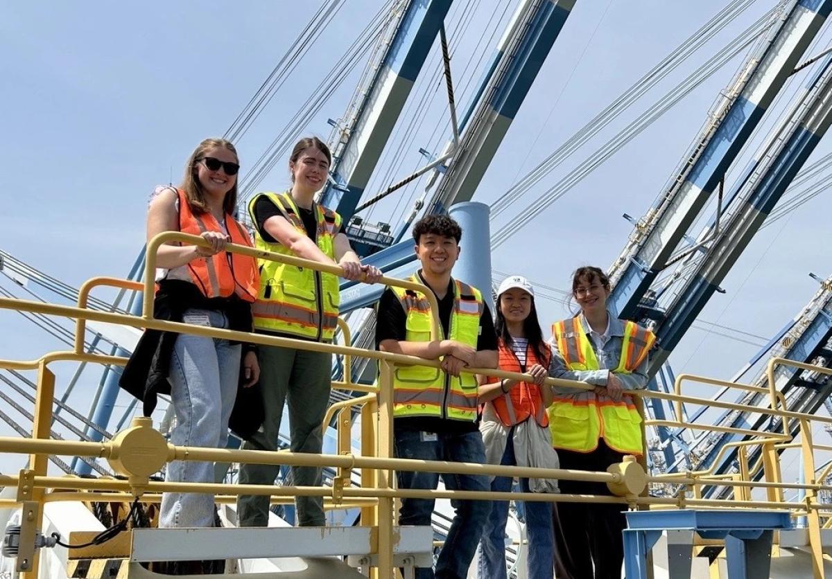 Five young people in safety vests stand on a crane.