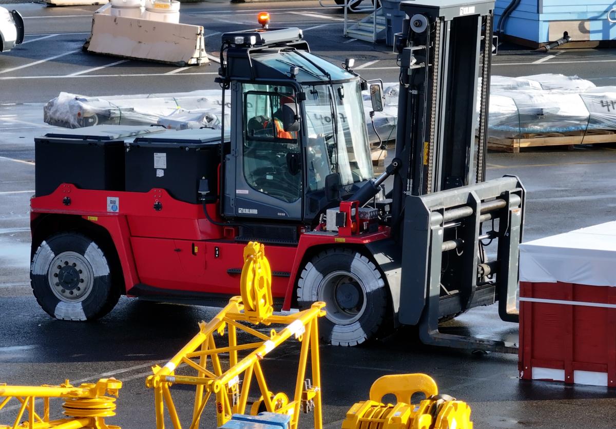 A red electric forklift works on a port terminal on a sunny day