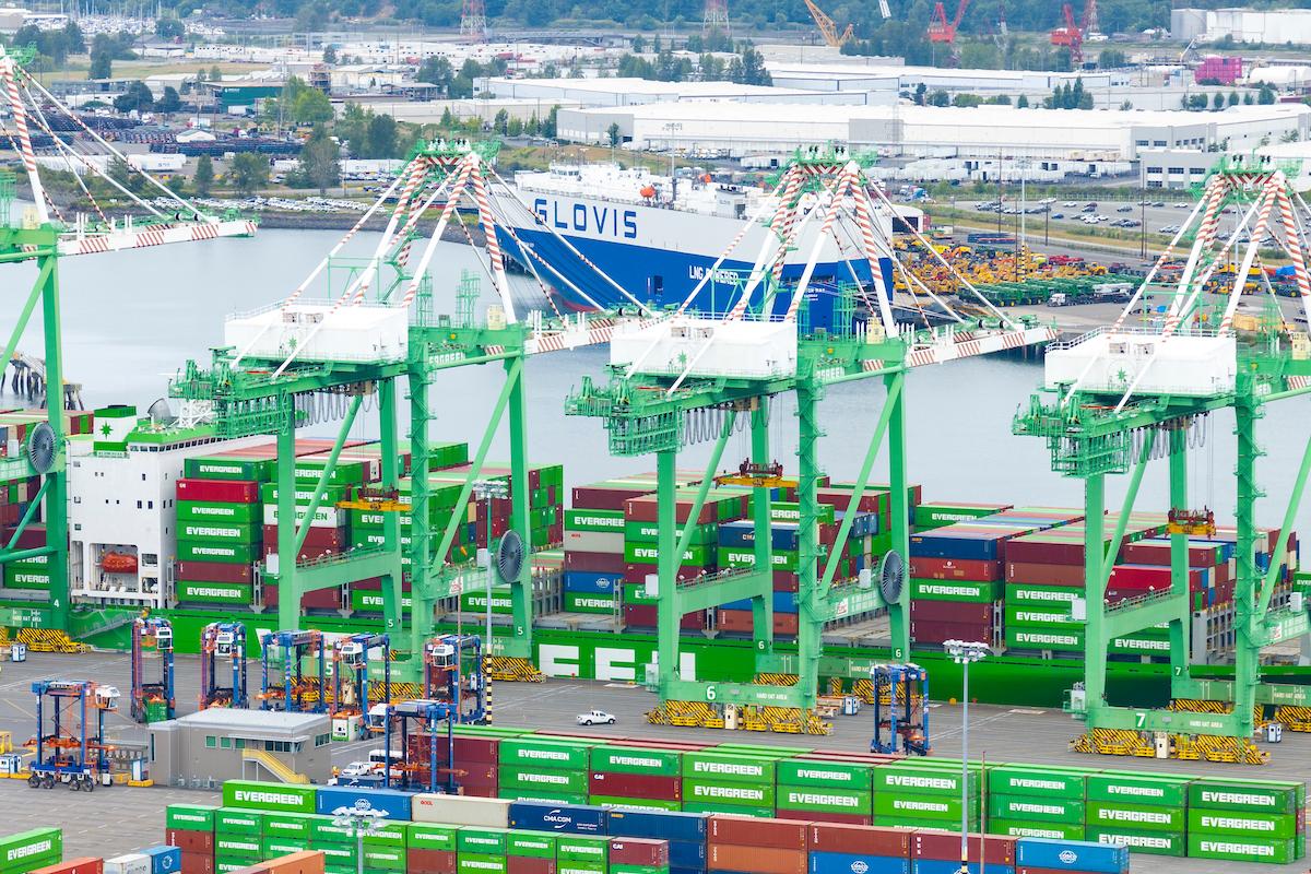 Drone shot of cargo operations and container ships at a Port with a ship in the background. 