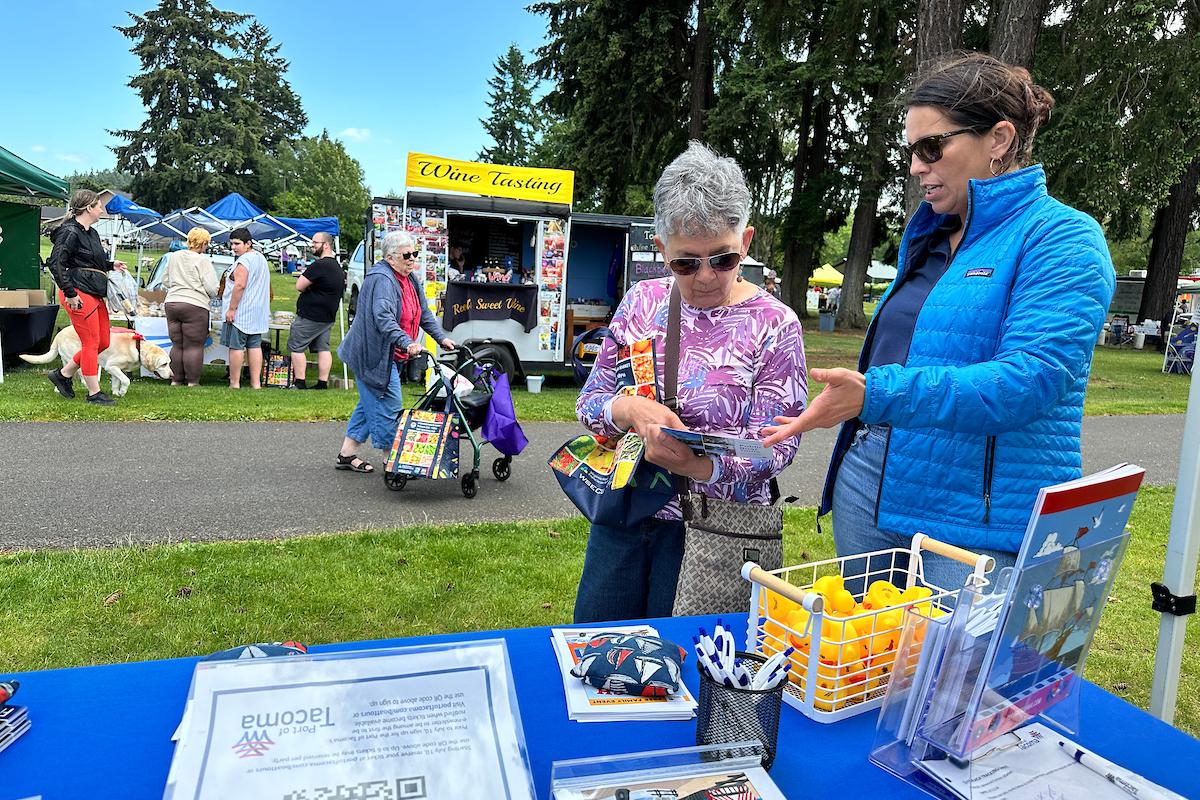 A woman in a blue coat talking to an older woman in a purple shirt at an event booth. 