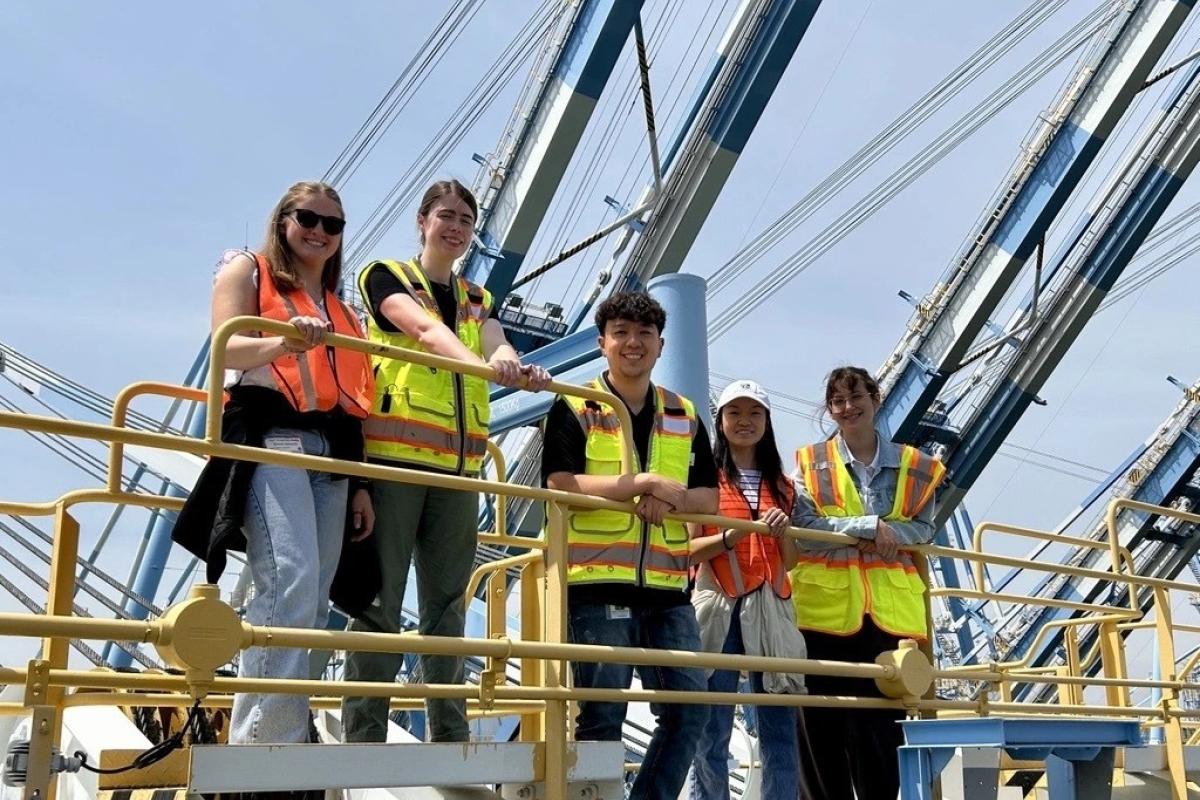 Five young people in safety vests stand on a crane.