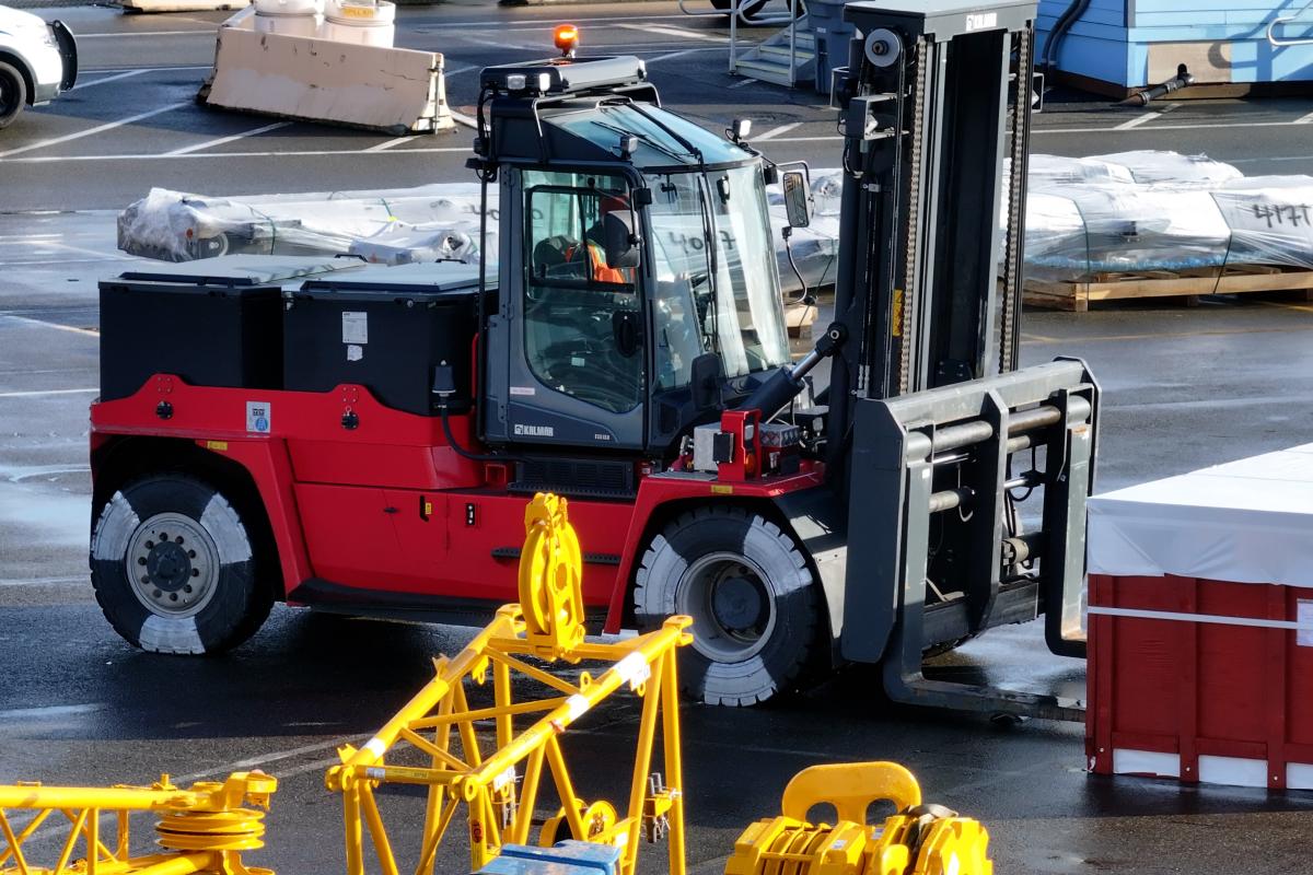A red electric forklift works on a port terminal on a sunny day
