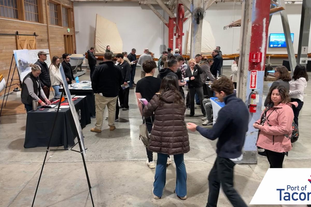 A group of people walk through an event filled with display booths. 