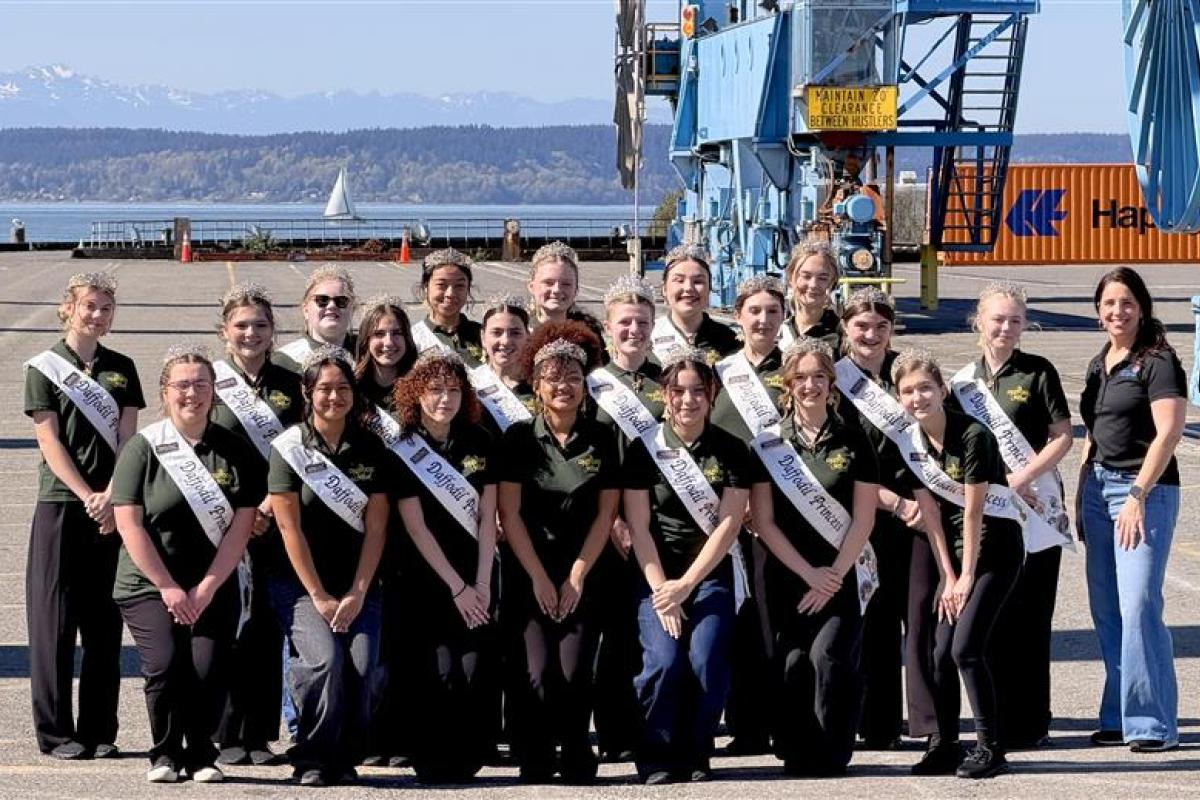 A group of Daffodil Festival princesses post on a port terminal with an employee.