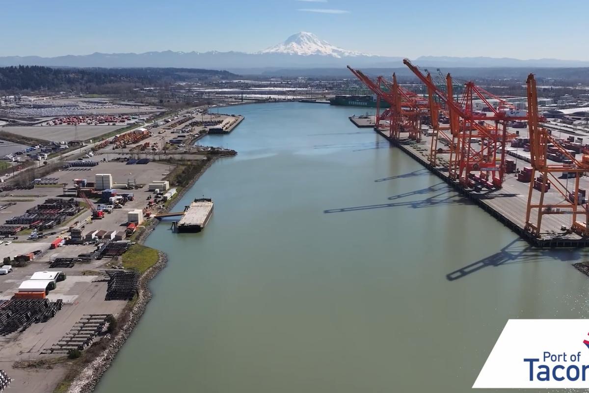 Aerial view of a port terminal with orange cranes over a waterway.