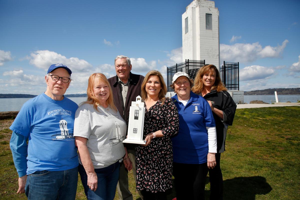 a photo of group of women and men holding a model of the lighthouse and smiling