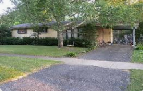 A single-story house at 1401 W Clarendon Ave, Phoenix features a front lawn, large tree, and a driveway leading to a covered carport. Shrubs line the front of the home, with a bicycle visible under the carport.