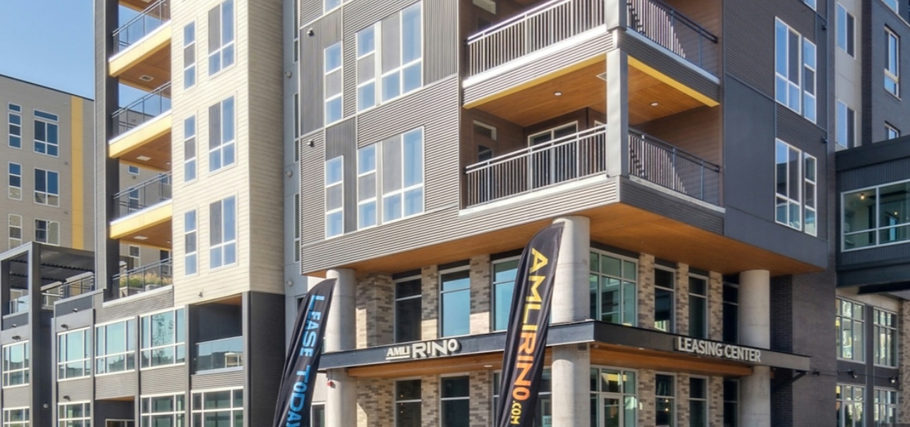 Modern Amli Art District Denver apartment building with large balconies and floor-to-ceiling windows. Two vertical flags and a sign indicate the presence of a leasing center at the entrance.