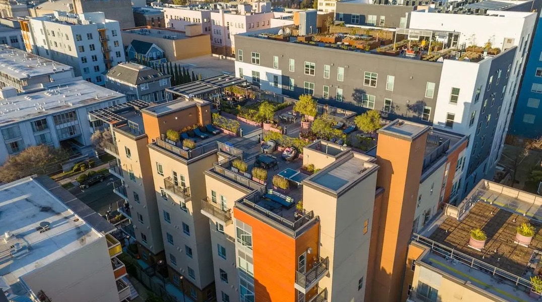 Aerial view of modern apartment buildings in Downtown Berkeley with rooftop gardens and terraces, featuring plants, outdoor furniture, and communal spaces near FOUND Study, surrounded by city streets and other residential structures.