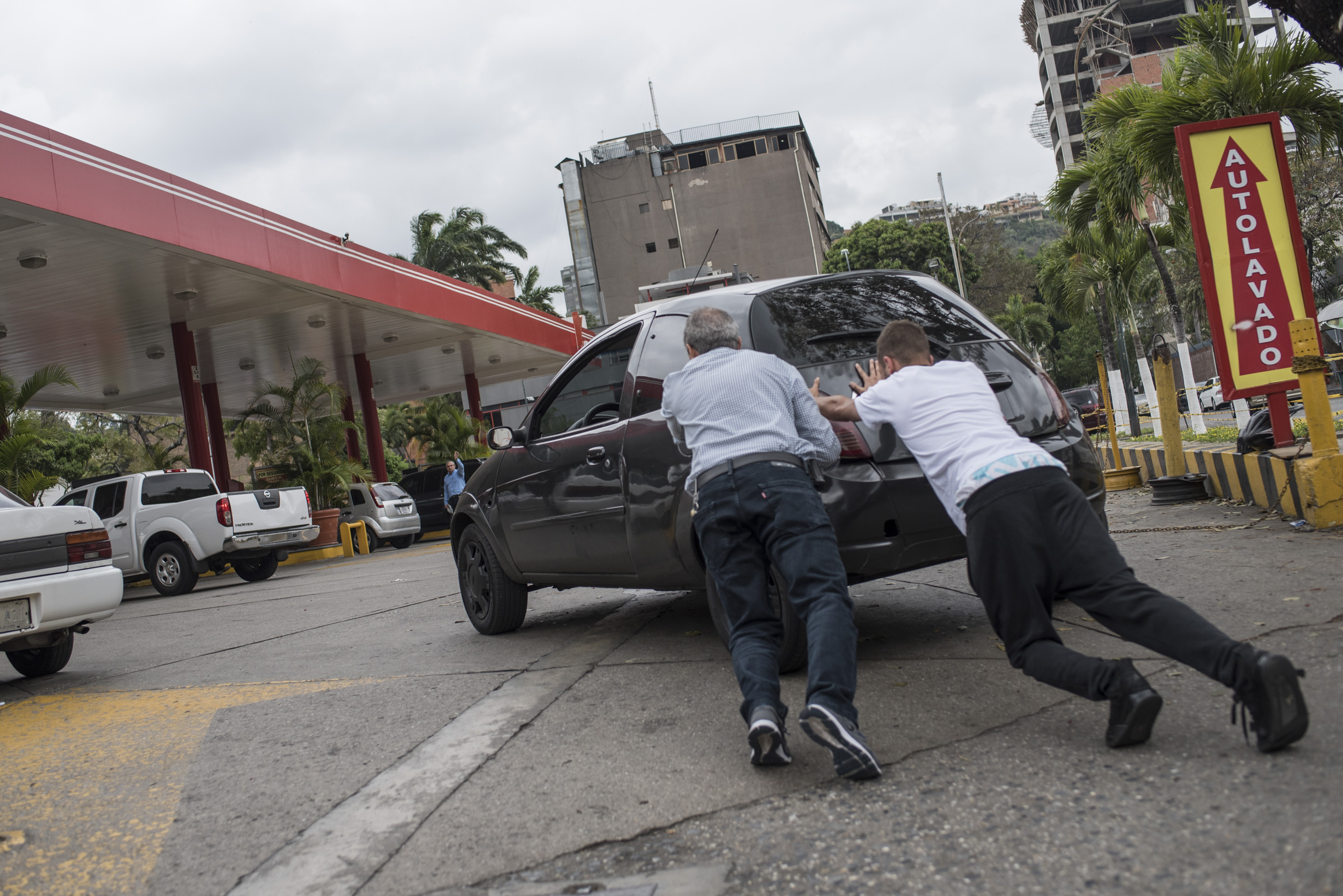 Dos hombres empujan un automóvil hacia una gasolinera en Caracas, Venezuela. Los conductores deben esperar largas filas para abastecerse en las gasolineras venezolanas, ya que un fallo en la distribución está afectando el suministro de combustible.LA PRENSA/AFP