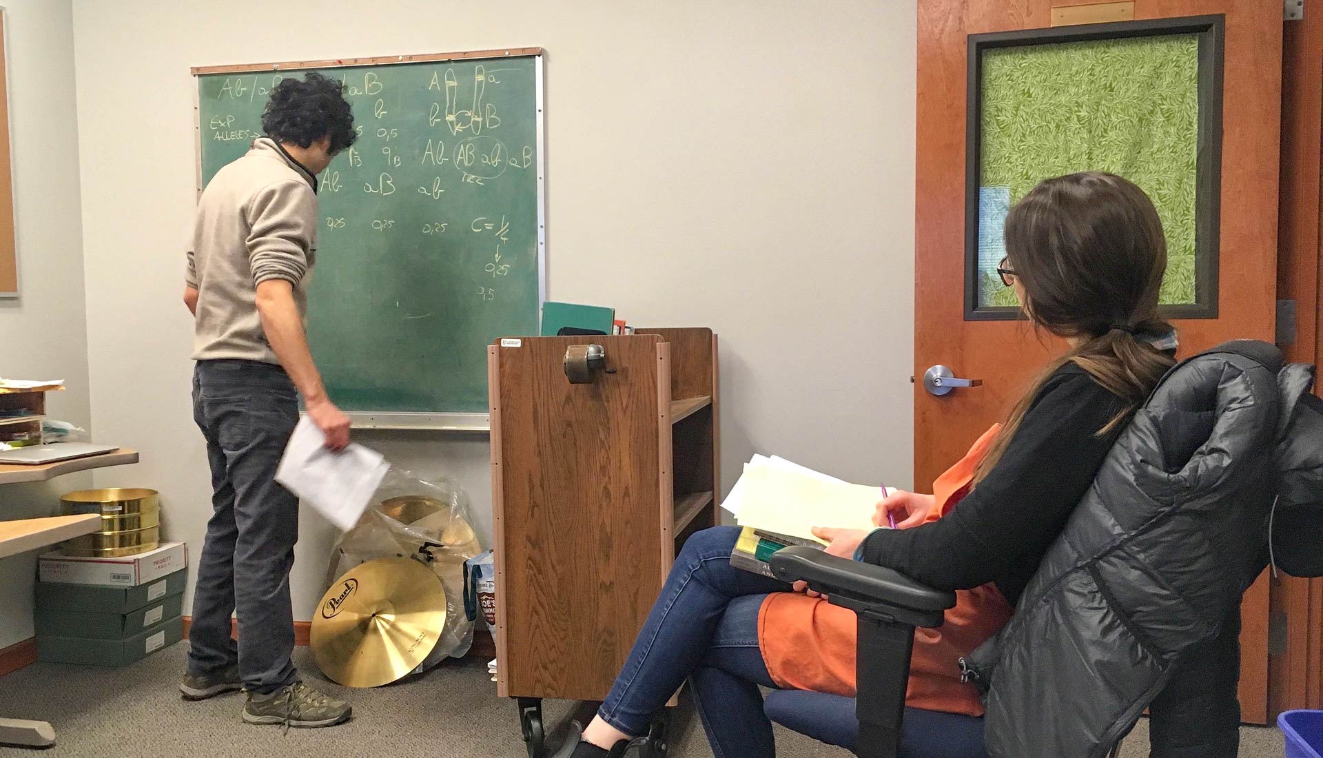 Young woman watches young man at blackboard