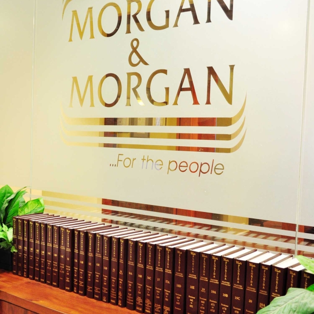 Office interior with "Morgan & Morgan" logo on a glass wall, framed by elegant gold lines.