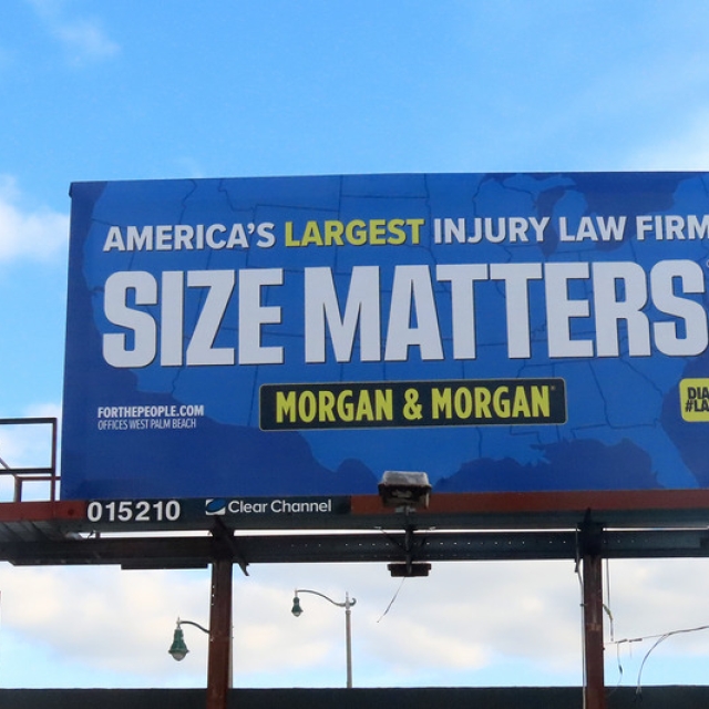 Billboard against a blue sky reads, "America's Largest Injury Law Firm. Size Matters. Morgan & Morgan" in bold text. Tone is assertive and promotional.