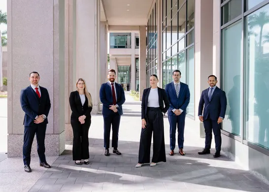 A group of six professionally dressed people stand outside a modern office building.