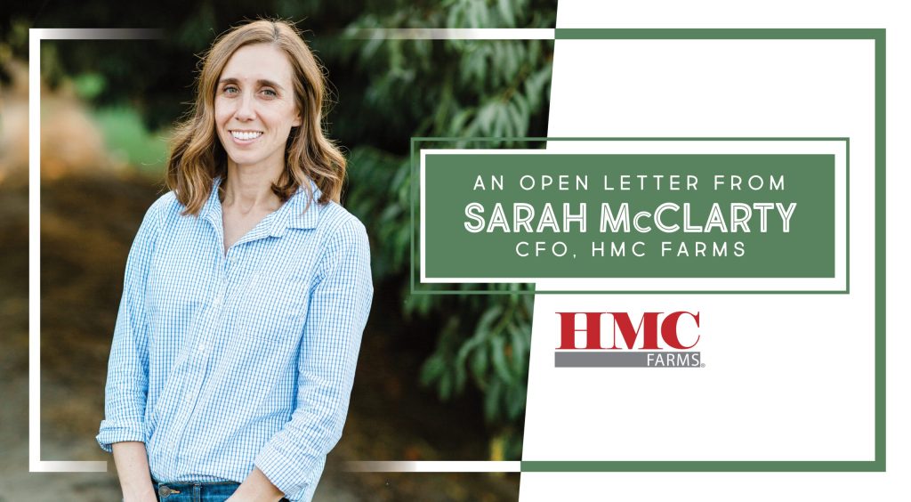 Sarah McClarty standing in a peach orchard wearing a blue and white checkered shirt