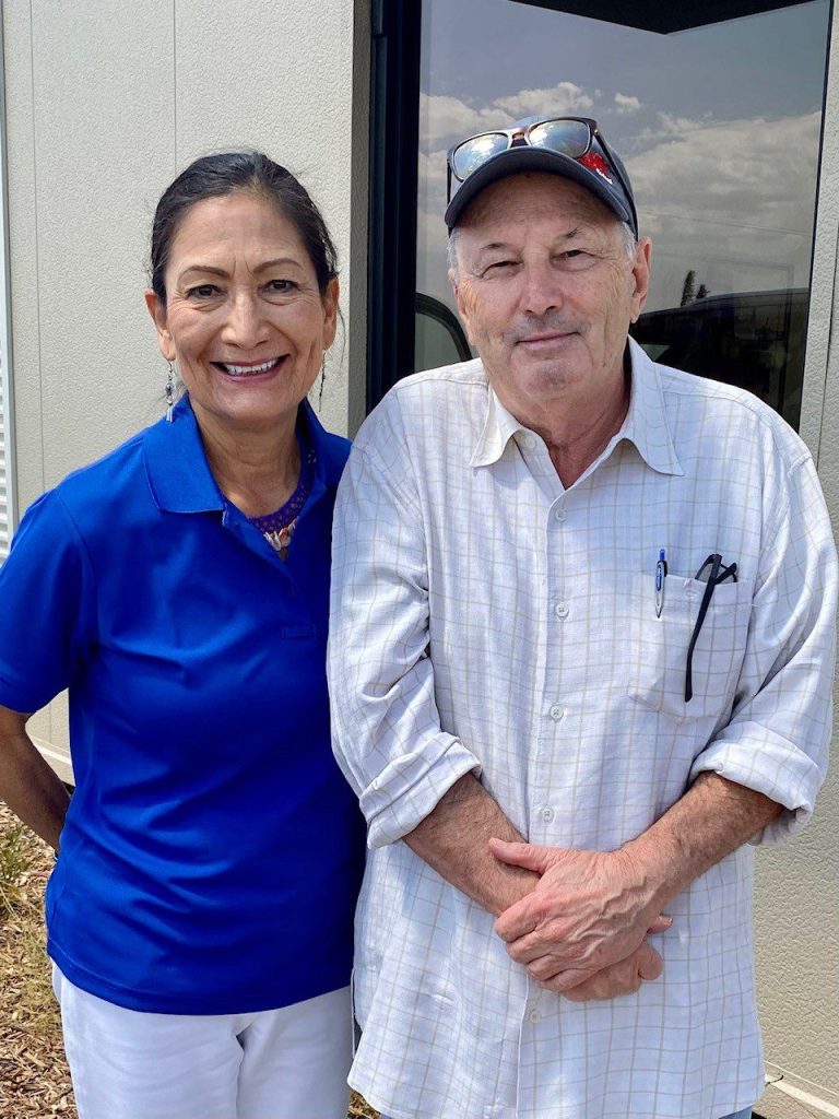 Woman with blue polo stands next to man with off white button up shirt and hat