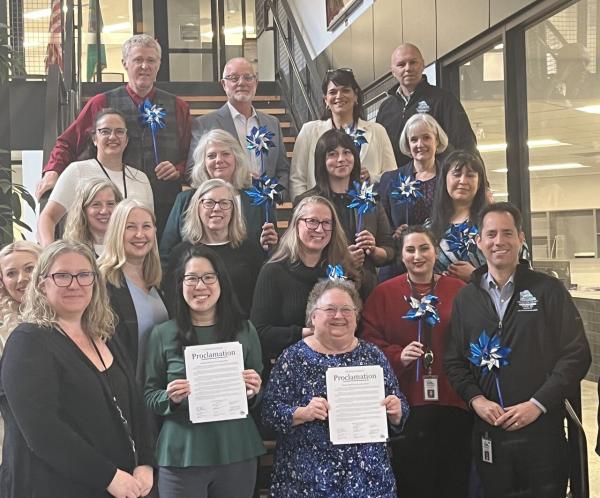 Thurston County Board of Health proclaiming April as Child Abuse Awareness Month. Standing on staircase, holding blue pinwheels 