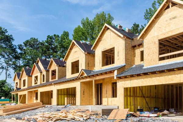 Row of new homes under construction with wood framing and dark roofs, showing various stages of residential development.