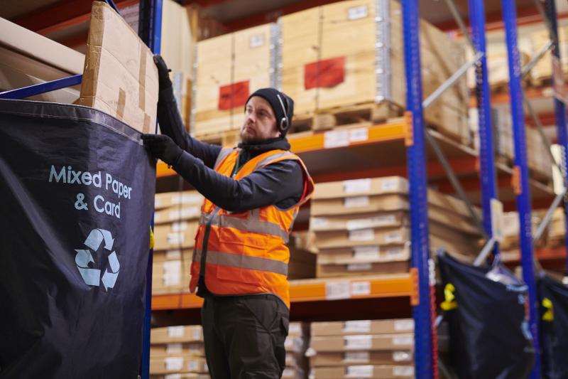 Man recycling cardboard in a warehouse setting.