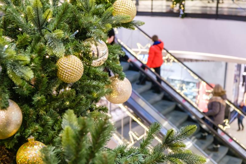 Golden Christmas balls and garland on a decorated fir tree in Shopping Mall. Blurred people on escalator, in festive business center