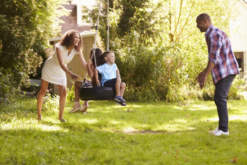 Parents Pushing Children On Tire Swing In Garden stock photo