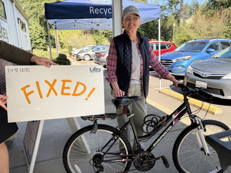 Picture of a woman with a bike and a sign that says "Fixed!"