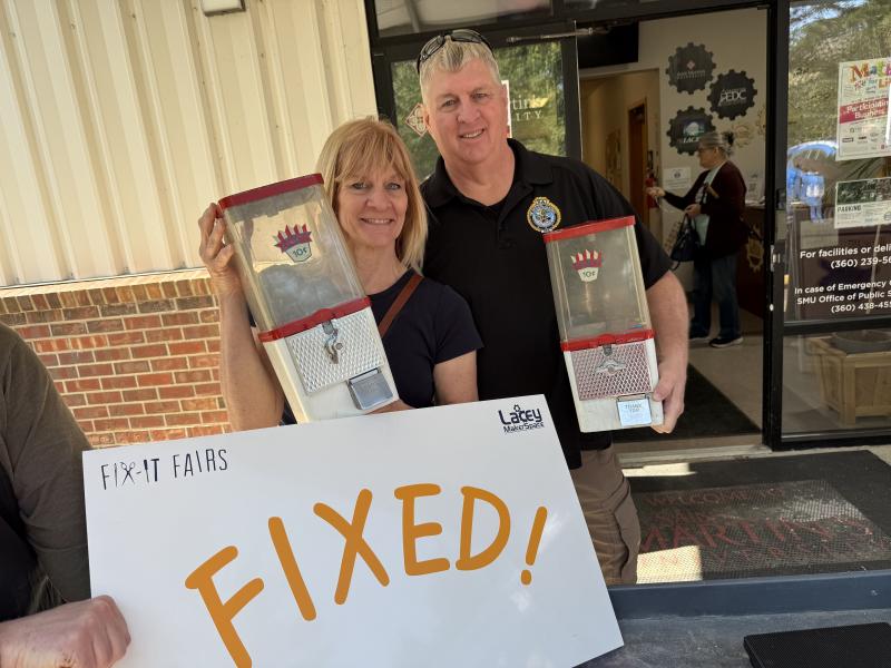 Photo of a couple holding 2 gumball machines and a sign that says "Fixed!"