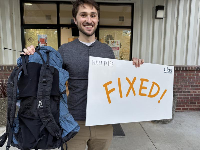 Photo of a young man holding a backpack and a sign that says "Fixed!"