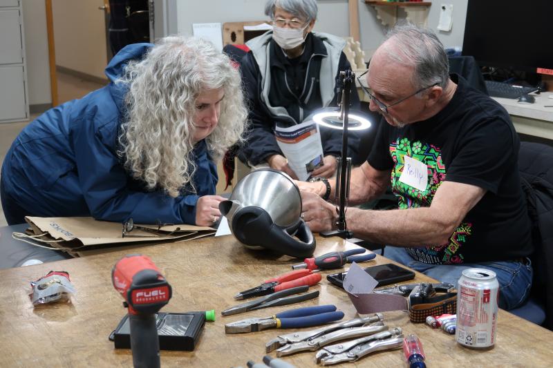 2 adults working on fixing a tea kettle.