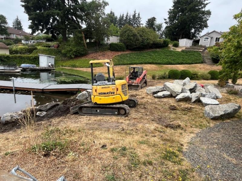 Yellow tractor moving dirt for boulders to sit along a shoreline
