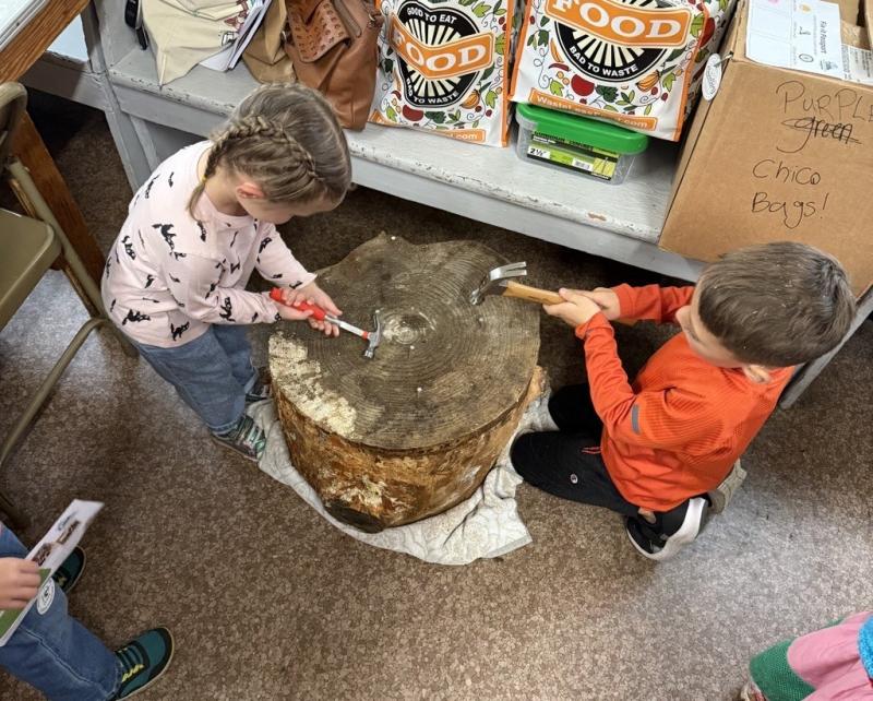 2 kids practicing hammering on a tree stump with nails.
