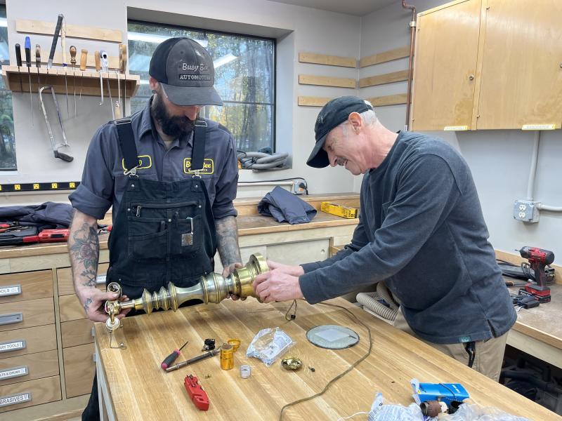 Two male volunteers stand at a table and repair a lamp together.