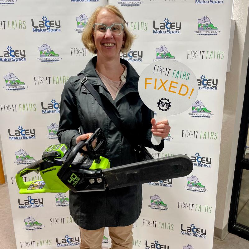 A woman poses with a repaired electric chainsaw.