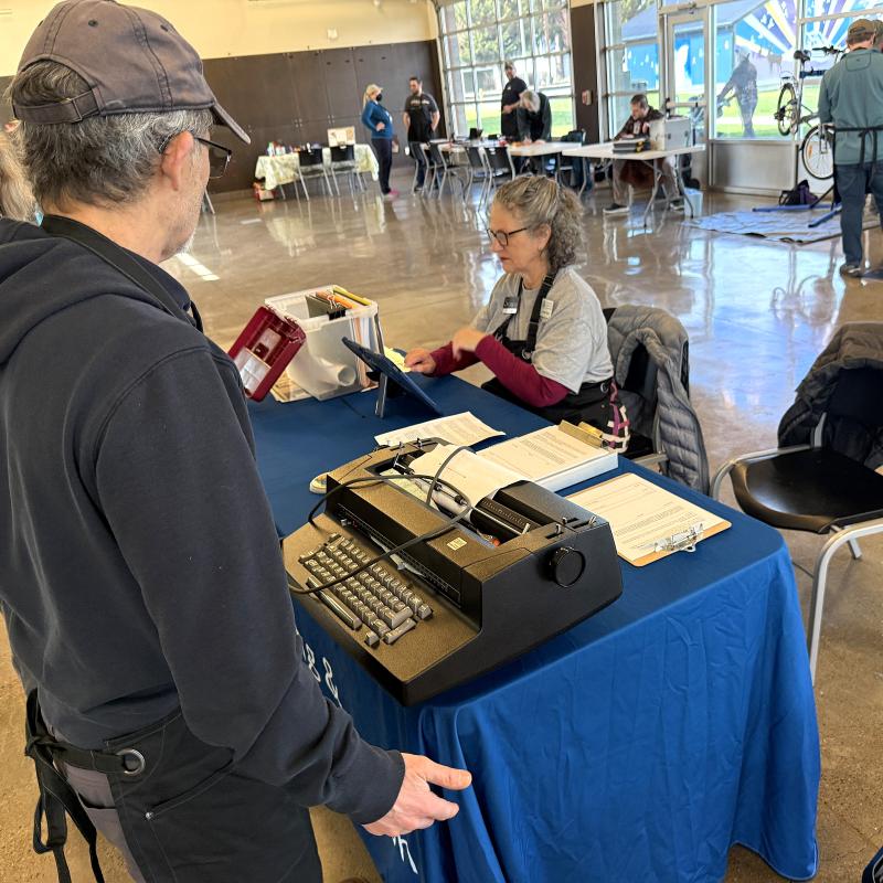 A man stands at a table with a typewriter.