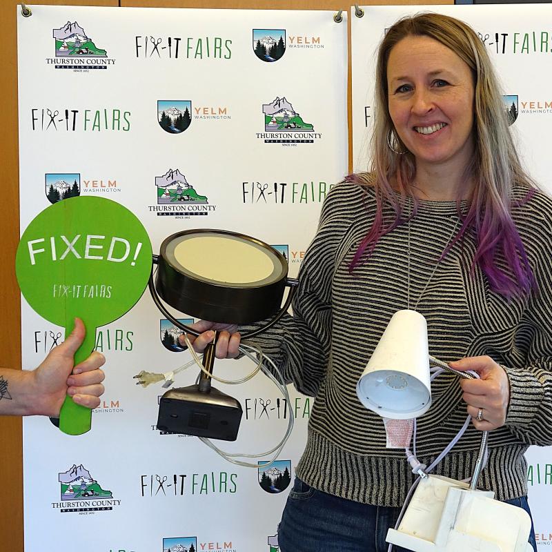 A woman holds a lamp and a mirror, with a sign that says Fixed.
