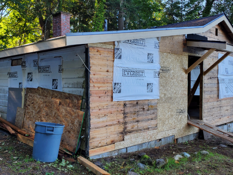 Single-story building with exposed plywood and white house wrap during renovation, illustrating a code enforcement case for work without permits.