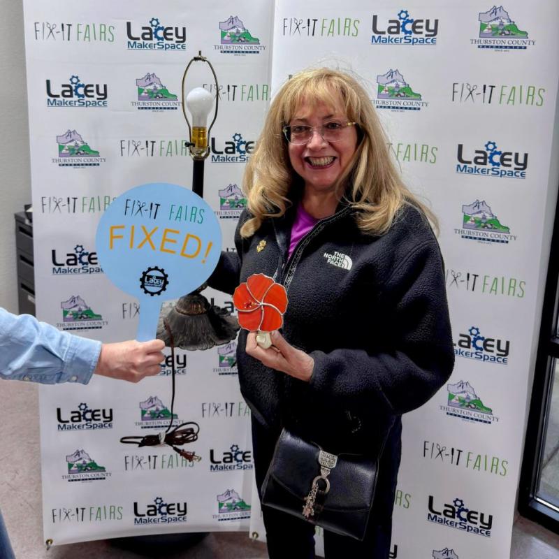 A woman holds a lamp and a sign that says Fixed.
