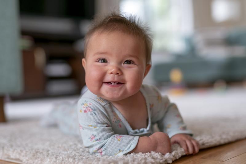 smiling baby laying down on indoor rug