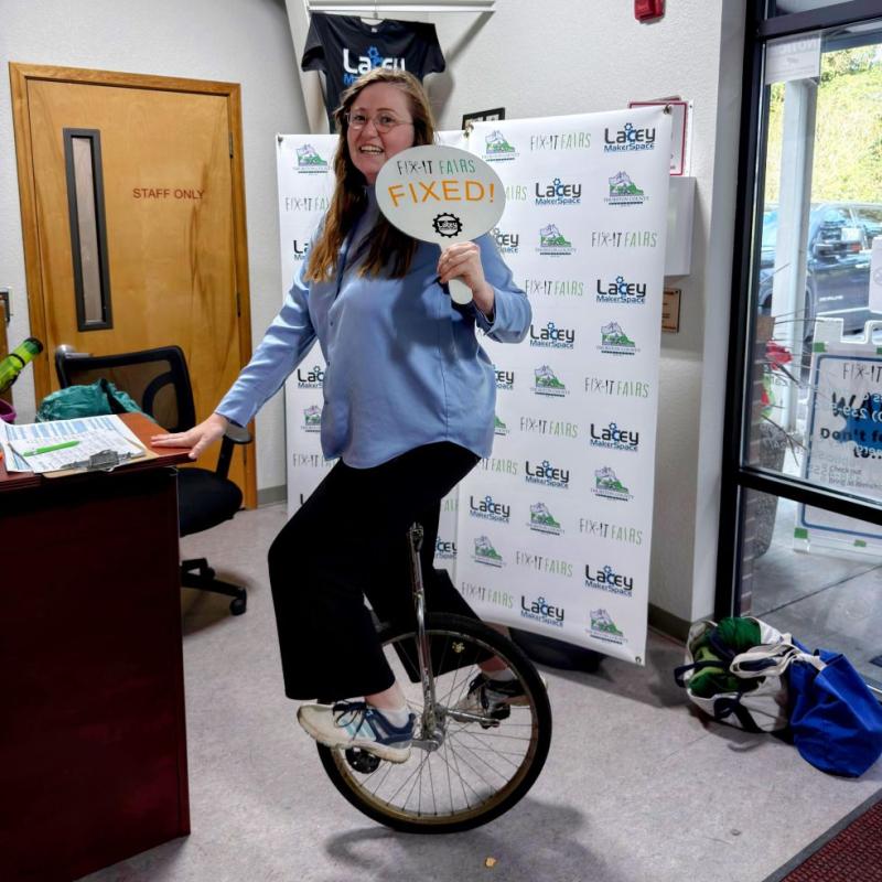 A women on a unicycle holds a sign that says Fixed.