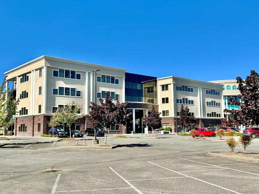 image shows two large modern, multistory office buildings connected by a glassed in breezeway in the center. the view is from the front of the building and its large parking lot on a sunny blue-sky day