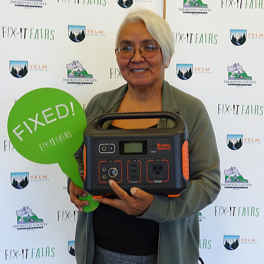 A person standing with a powerbank and a sign that says Fixed.