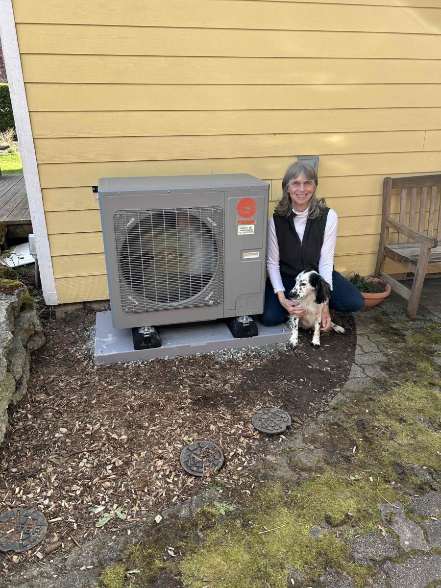 A community member poses with her dog for a photo next to her newly installed Heat Pump unit beside her yellow-painted house as part of the grant-funded Energize Thurston program.