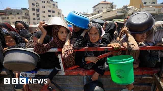 Many women hold out bowls and buckets for aid, some using the empty buckets to shake their faces from the sun.