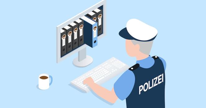 Ein Polizist ist an einem Laptop, auf dem mehrere Papierordner zu sehen sind mit einem Gesicht darauf.