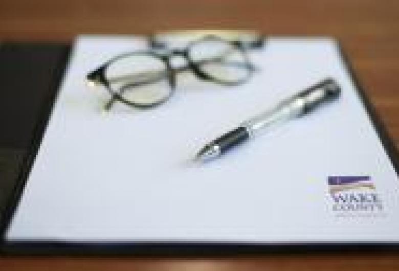 Glasses, a pen and Wake County letterhead rest on a table